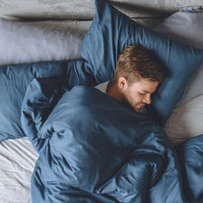 A young adult male sleeping comfortably in a bed