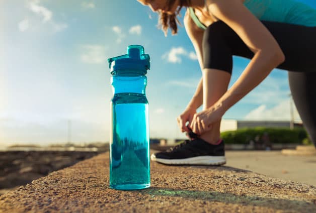 Woman lacing shoes next to water bottle, getting ready for run