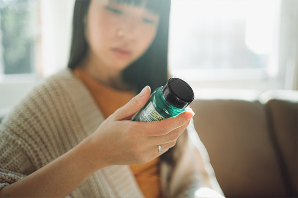 Young woman reading a supplement bottle label while seated on a couch
