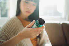 Young woman reading a supplement bottle label while seated on a couch