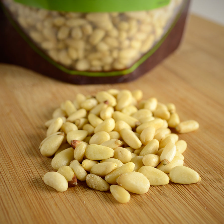 NWF1142 | pile of shelled pine nuts on a wooden cutting board with a resealable pouch in background