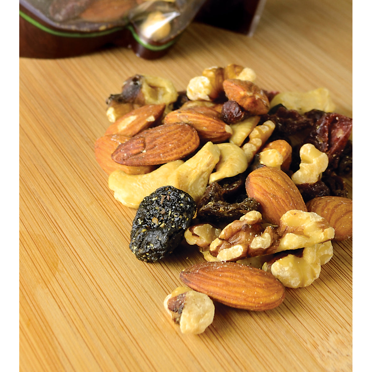 NWF1195 | mixed nuts and dried fruit on a wooden cutting board showing almonds, walnuts, cashews, and raisins