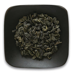 FNP082 | Top-down view of rolled green tea leaves in a dark square dish