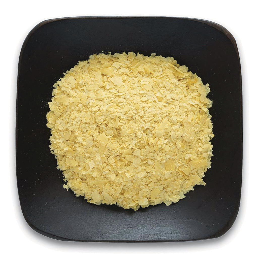 FNP021 | Pile of yellow nutritional yeast flakes on a black square plate - Thumbnail