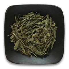 FNP086 | Loose green tea leaves on a square dark plate, top view