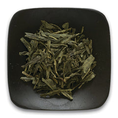 FNP084 | loose green tea leaves on a square black dish, top-down view