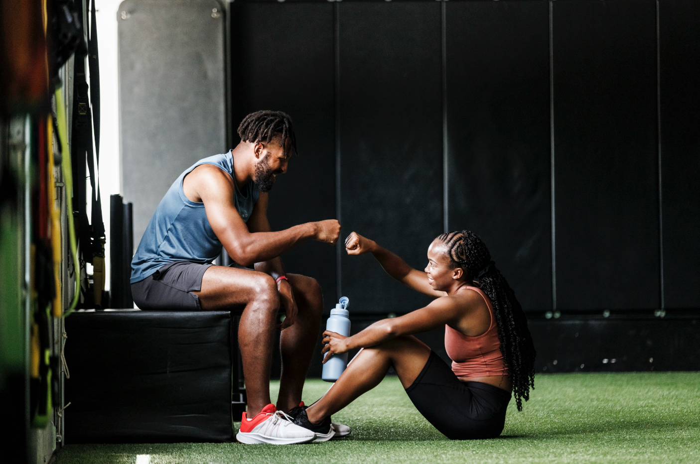 Man and woman in athletic wear sitting on the gym floor.