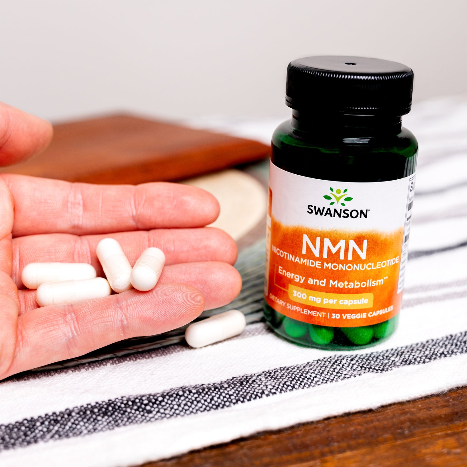SW1819 | Swanson NMN bottle beside a hand holding veggie capsules