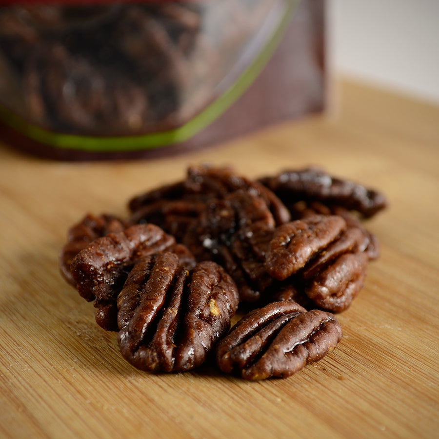 NWF1208 | glazed pecan halves on a wooden cutting board with a blurred bag in the background