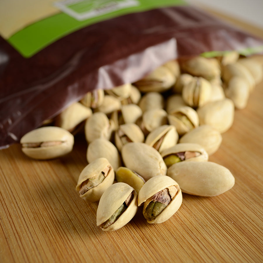 NWF1143 | close-up of pistachios spilled from a partially visible bag on a wooden board showing shells and green kernels - Thumbnail