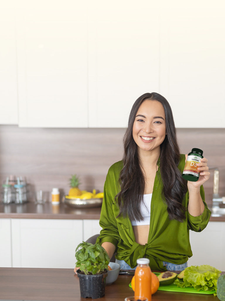 Woman holding a bottle in a kitchen with vegetables and a smoothie on the counter