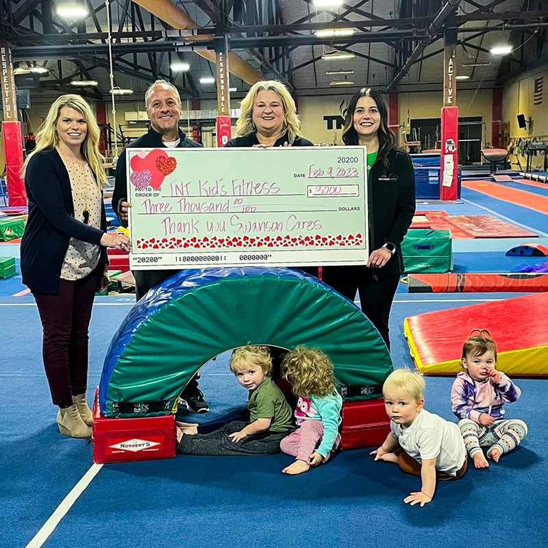Donation check presented to TNT Kids Fitness with children playing and looking at the camera