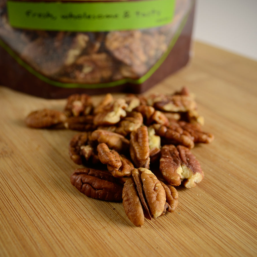 NWF1179 | shelled pecans scattered on a wooden cutting board with the product pouch blurred in the background