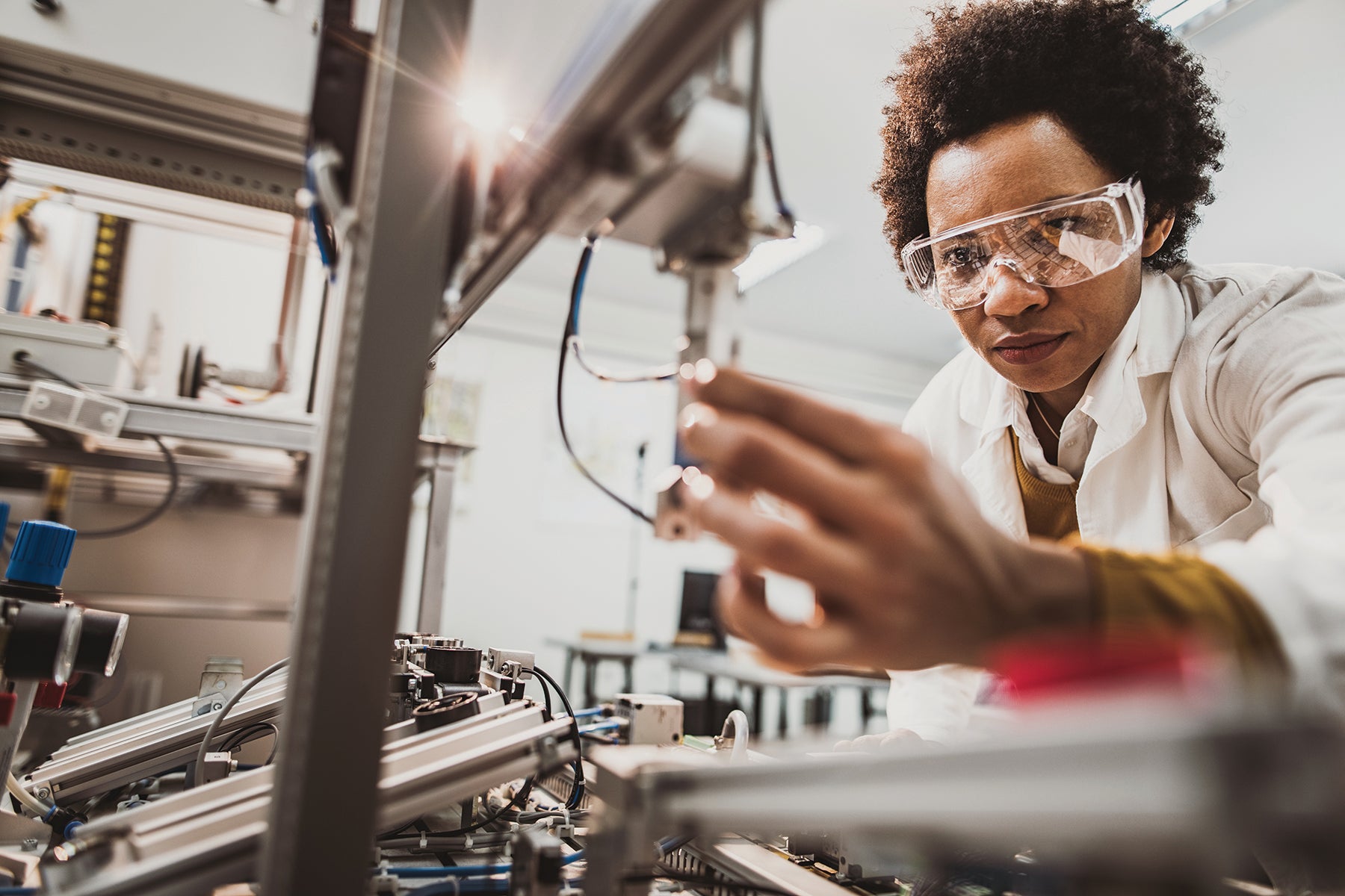 Scientist wearing safety goggles and a lab coat adjusting equipment inside a laboratory