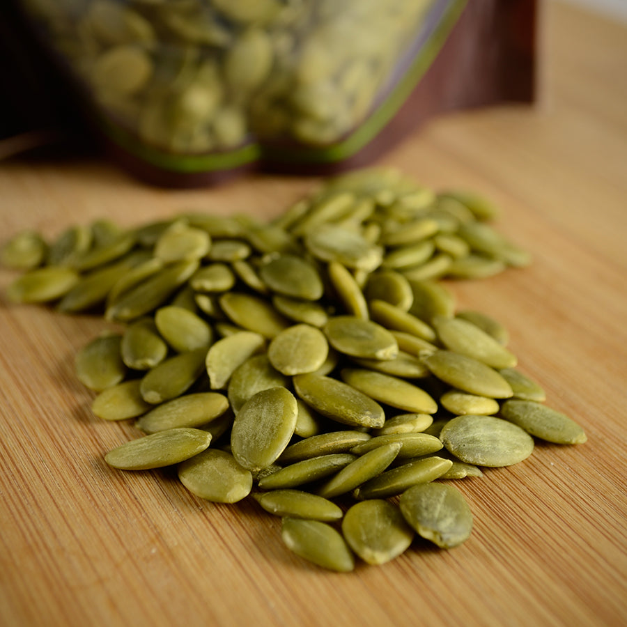 NWF1110 | pile of pumpkin seeds (pepitas) on wooden cutting board with resealable bag in background