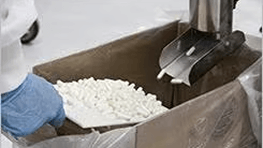 Person handling white powder in a container with a metal scoop.