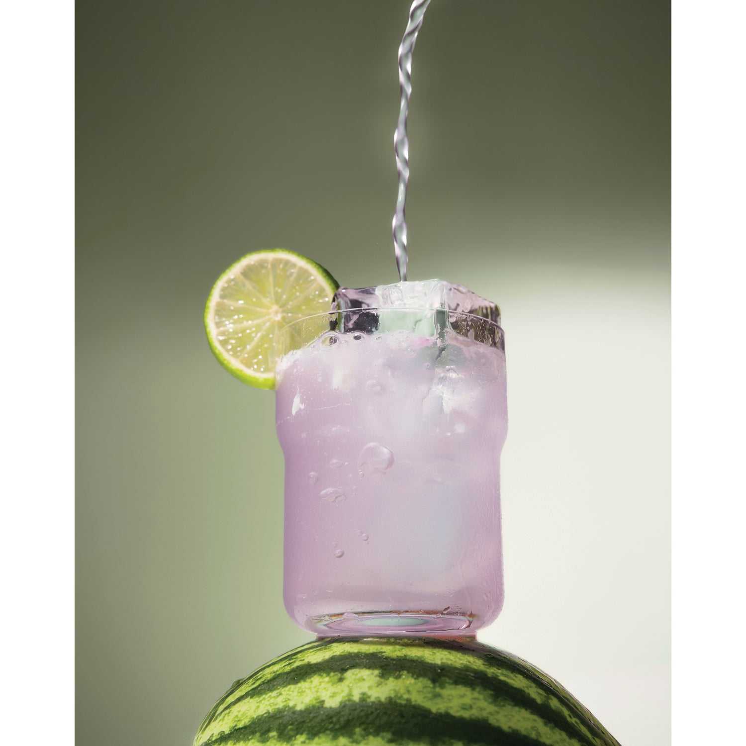 KTO003 | Pink drink poured into a glass with ice and a lime garnish on a watermelon