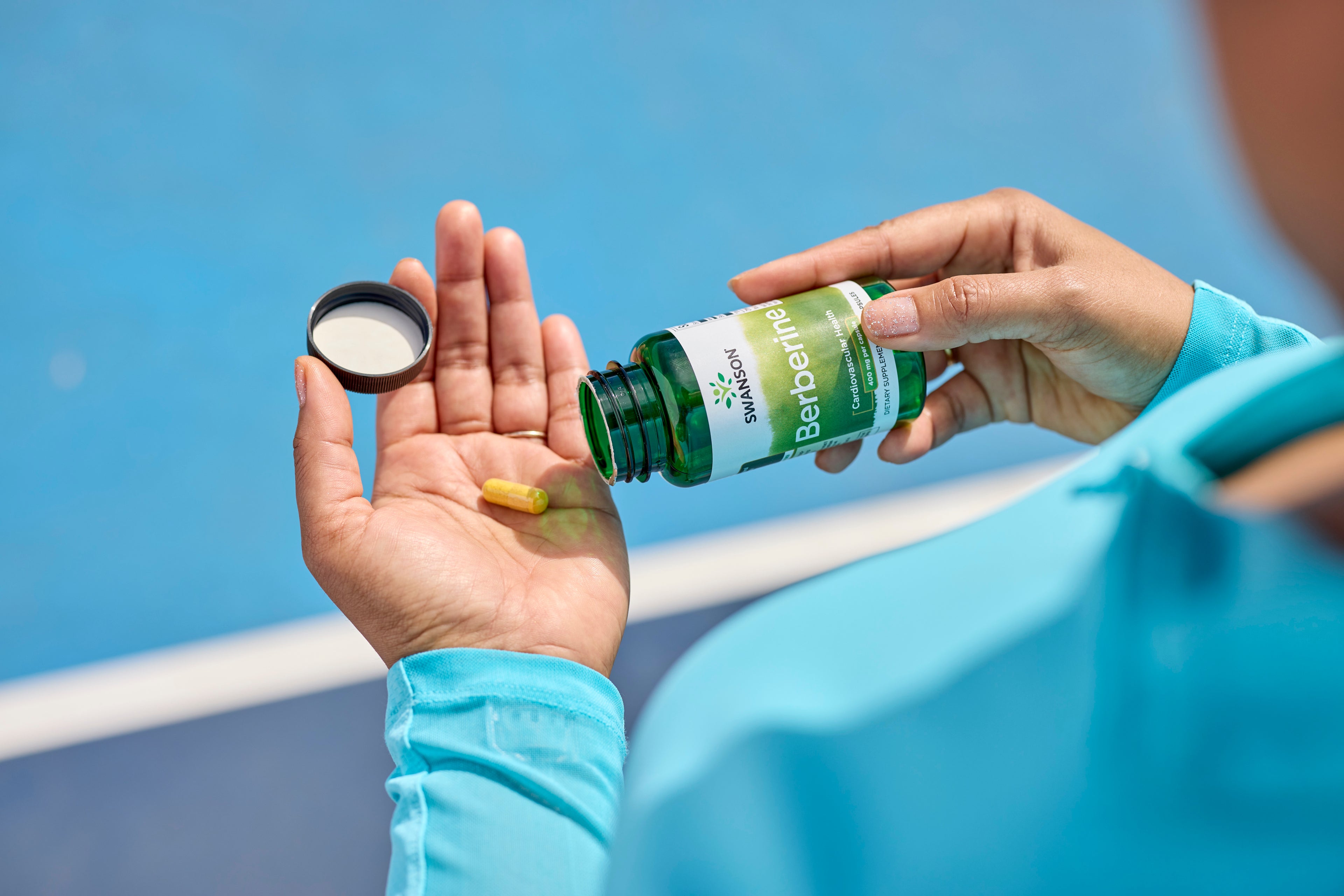 Person in a light blue shirt pouring a yellow capsule from a Swanson Berberine supplement bottle into their hand