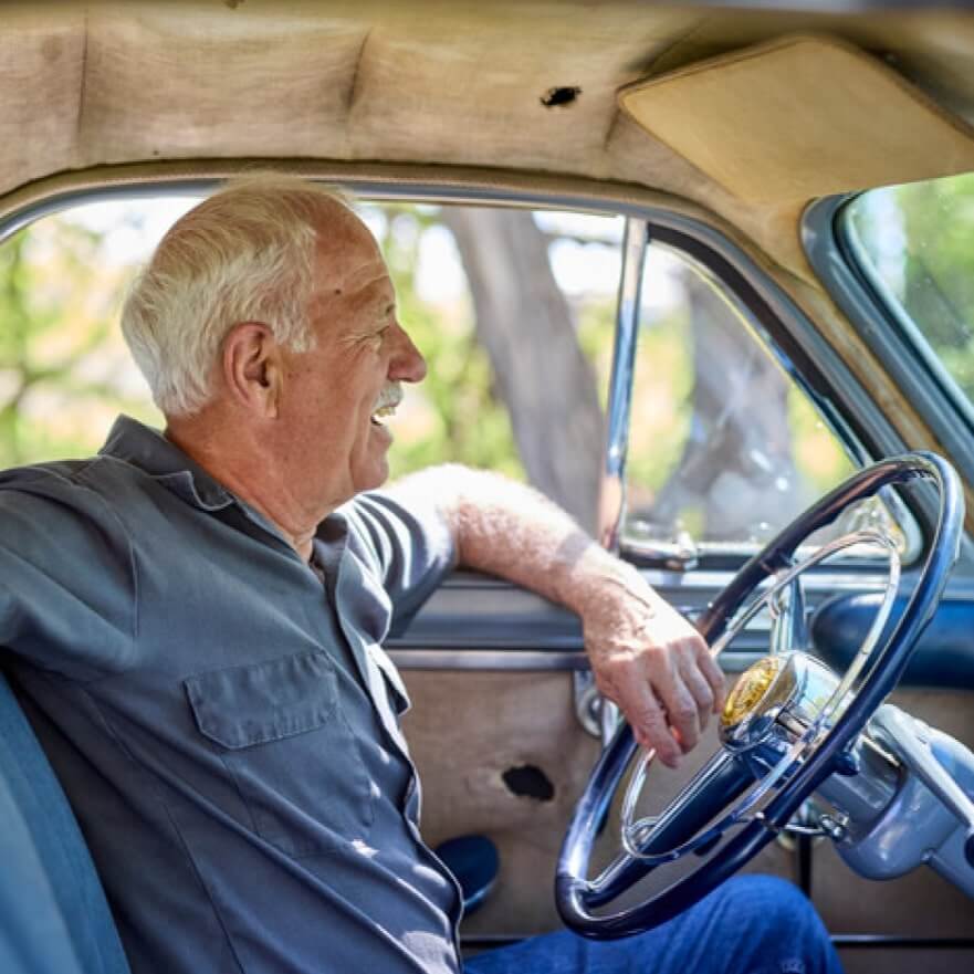 Man sitting inside a vintage car with a steering wheel