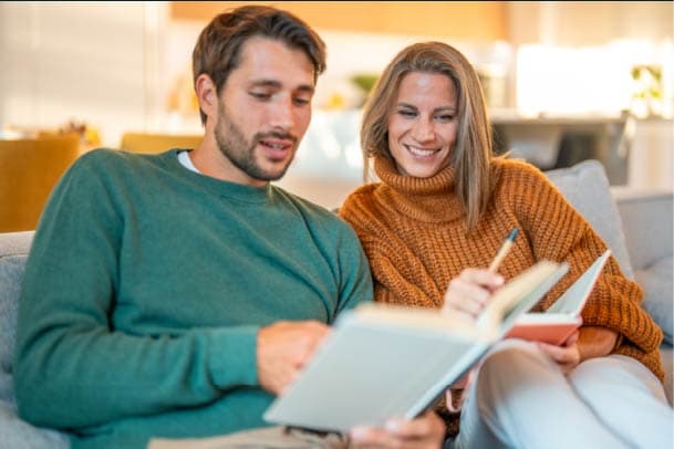 A man and a woman are reading from a book and taking notes